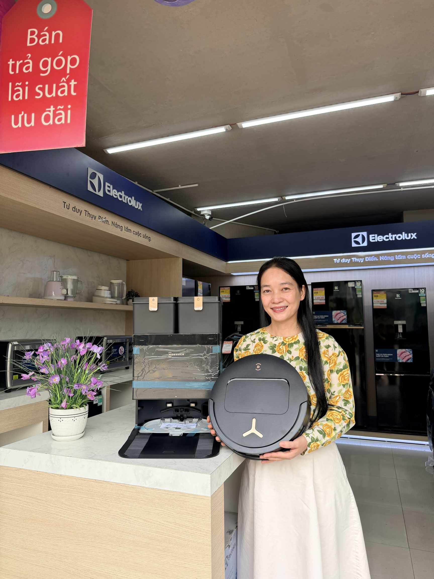 Người phụ nữ cầm robot hút bụi lau nhà tròn màu đen tại cửa hàng Electrolux